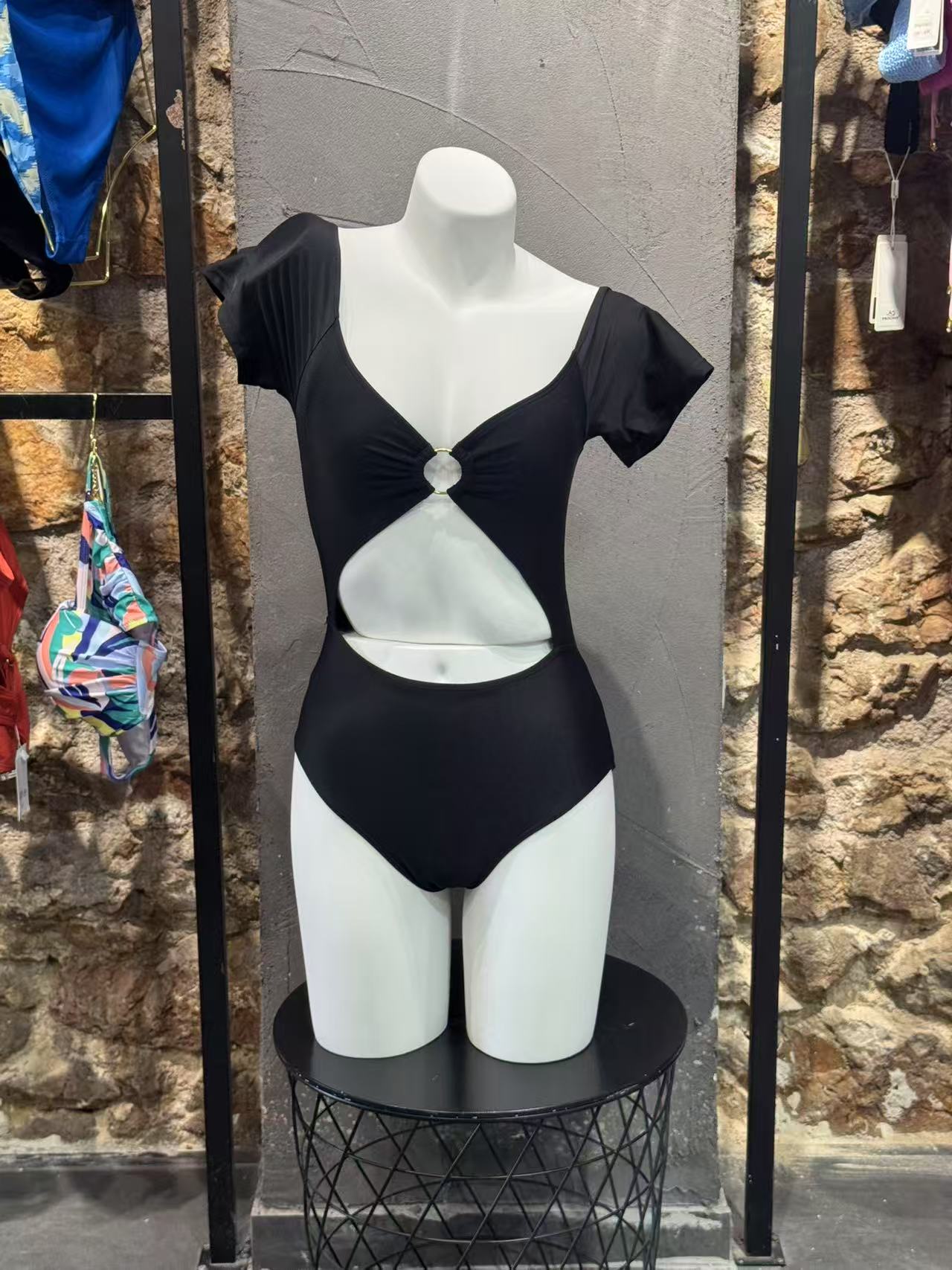 Black and white swimsuit on a mannequin against a stone wall.