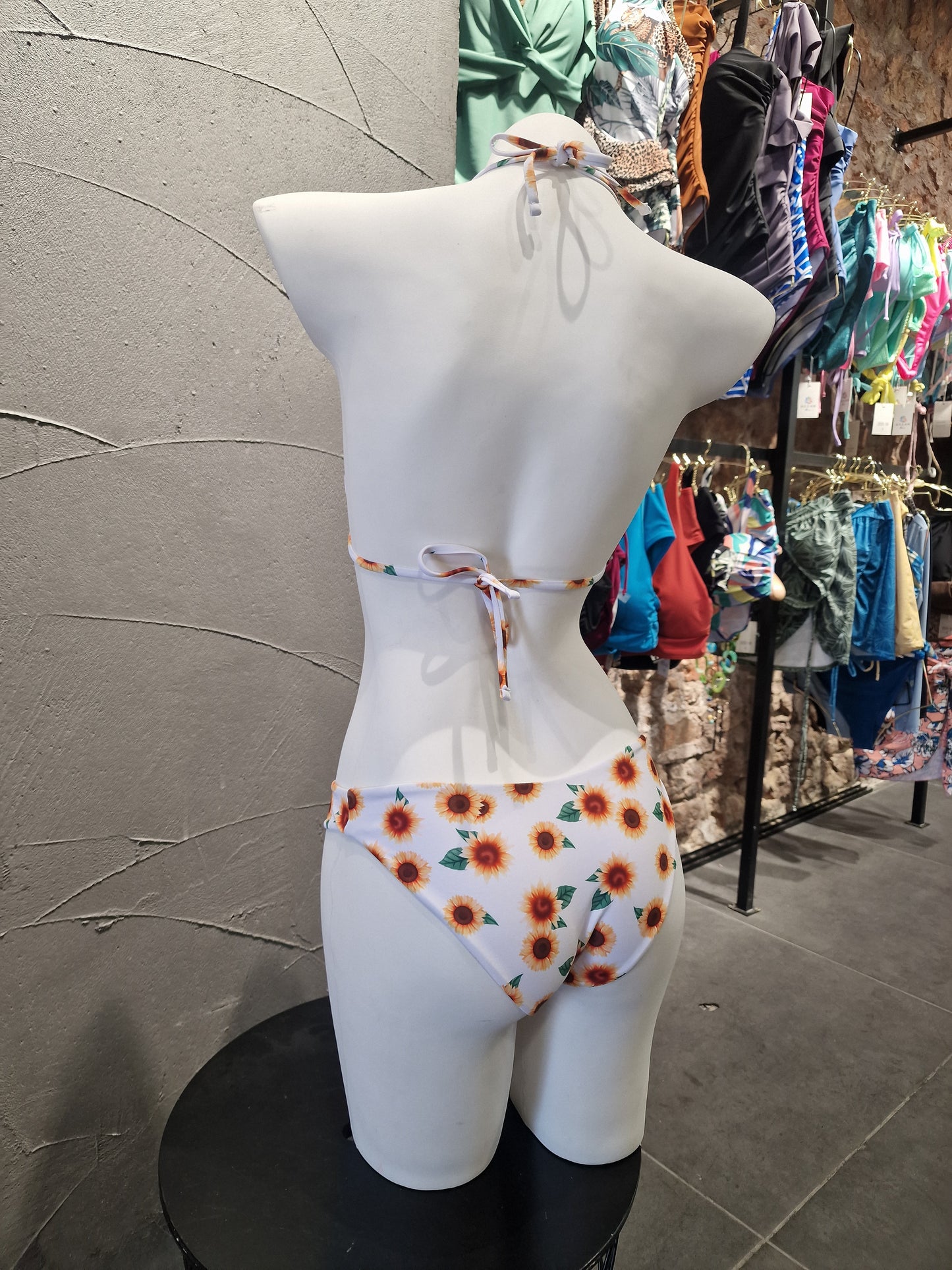 Mannequin wearing a floral-patterned dress with a blurred background of clothes on tables.