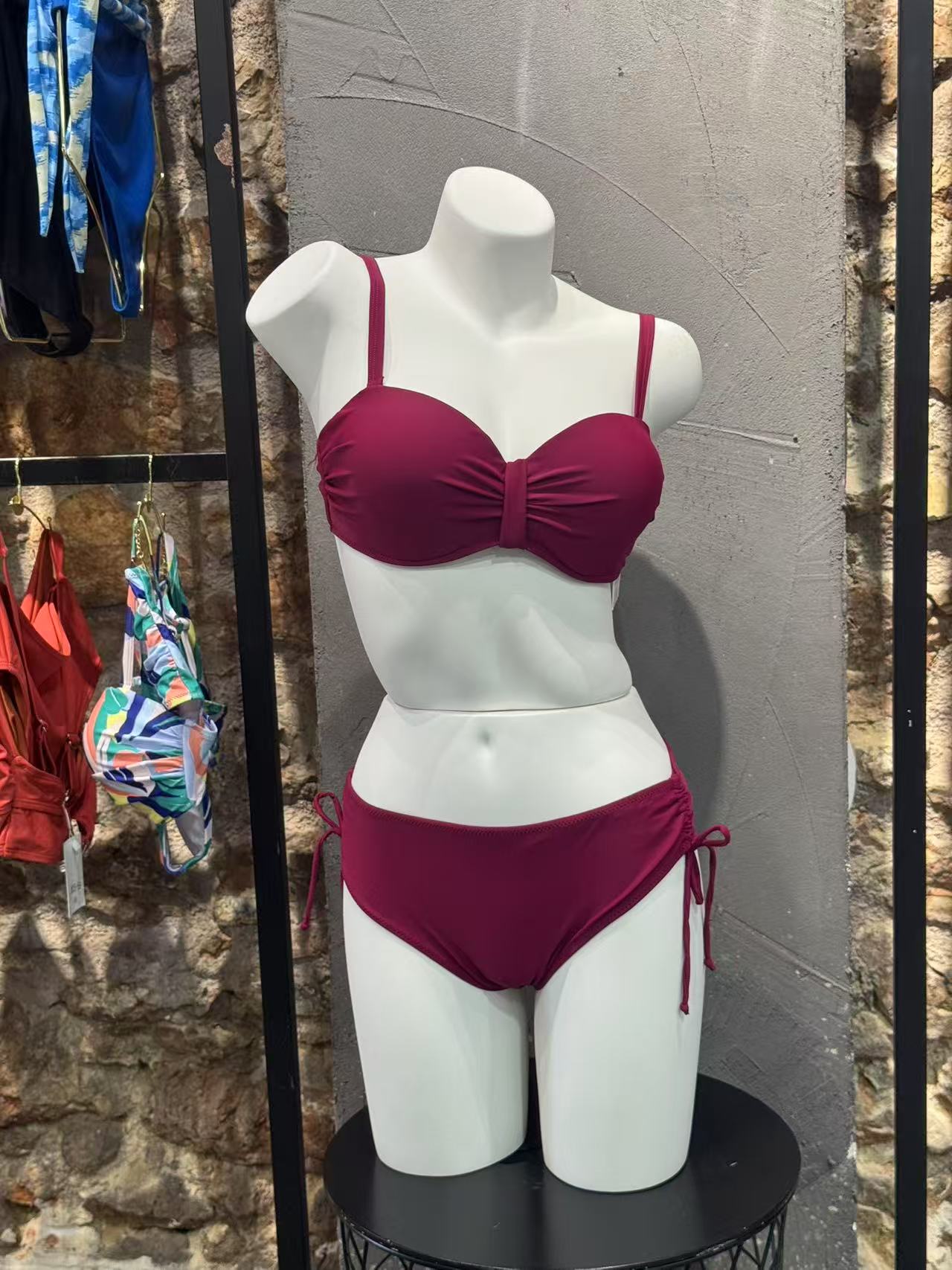 Mannequin wearing a maroon bikini set against a stone wall.