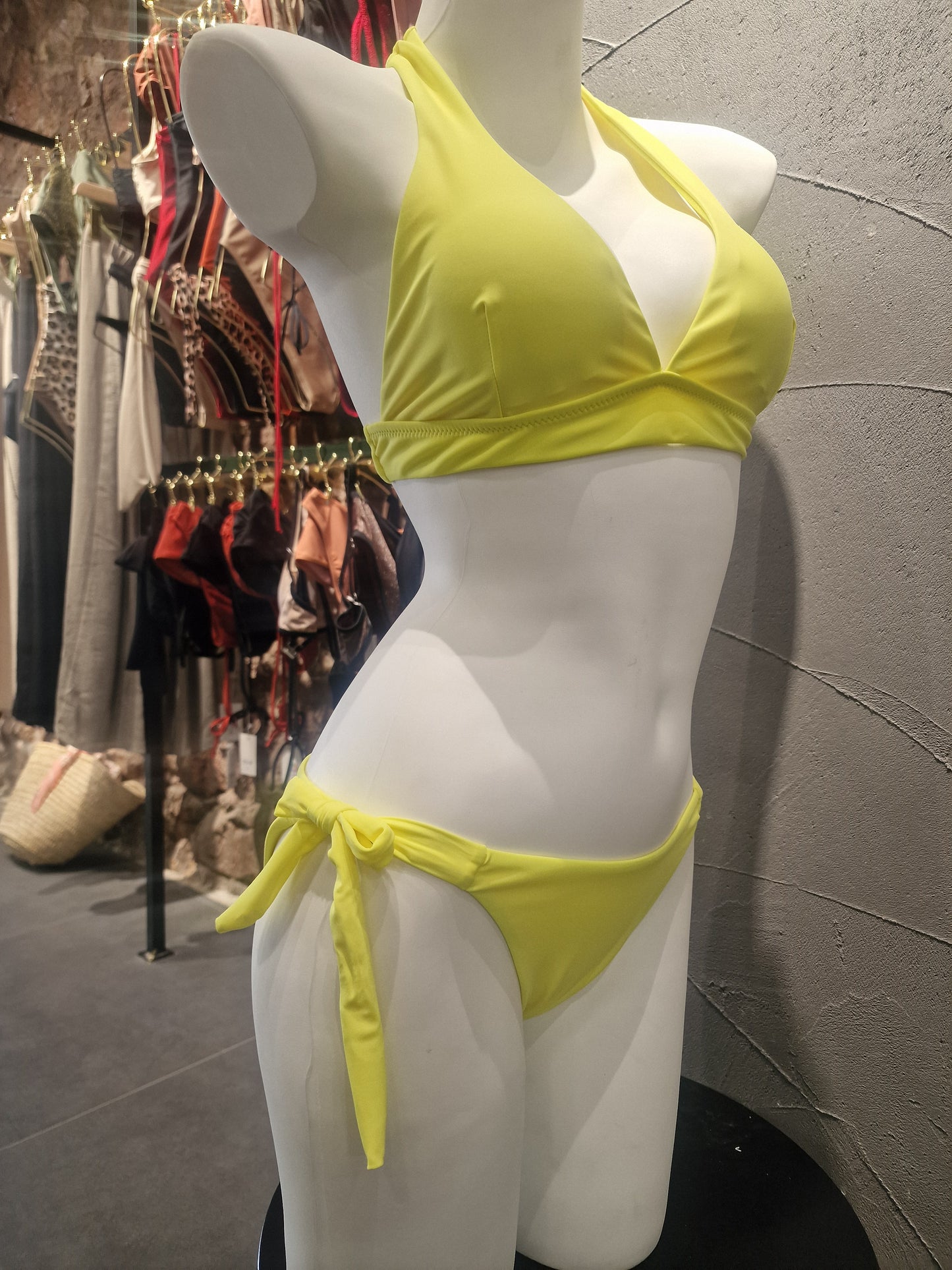 Mannequin wearing a yellow bikini top on a reflective surface with a patterned background