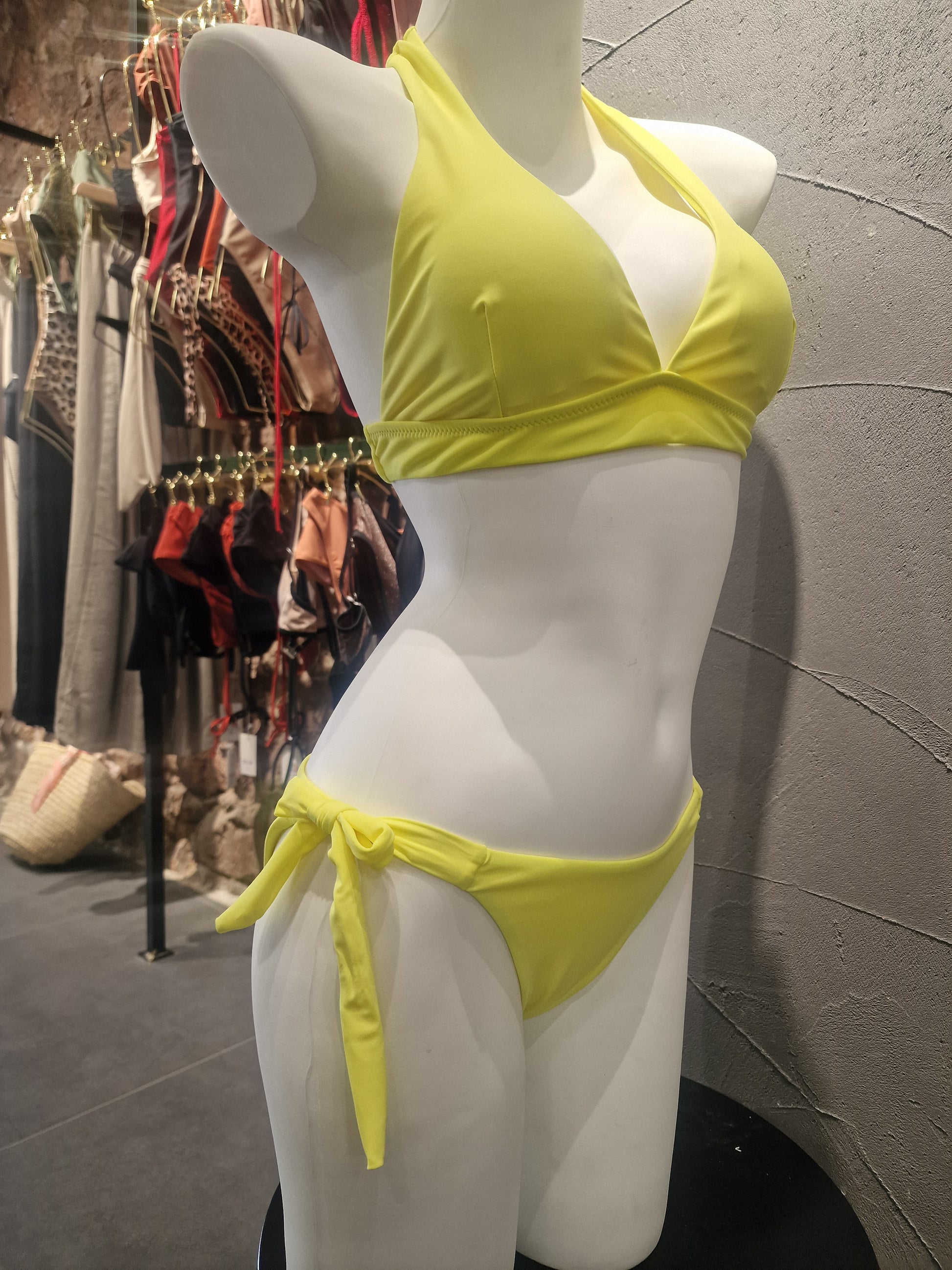 Mannequin wearing a yellow bikini top on a reflective surface with a patterned background