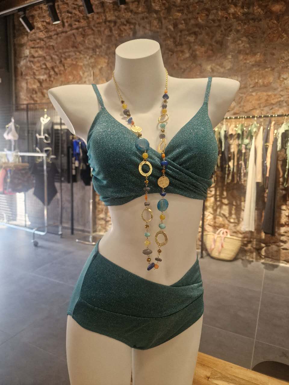 Mannequin wearing a green bikini set with a necklace in a store setting