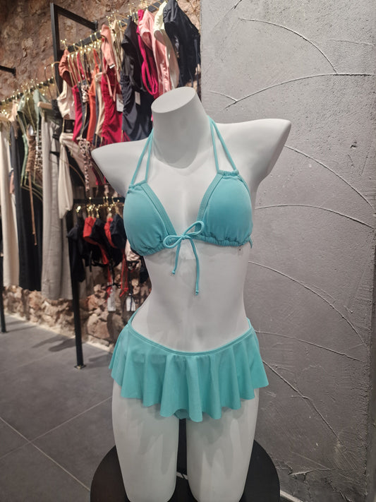Turquoise bikini top on a mannequin bust with white ruffled garment against a gray tiled floor.