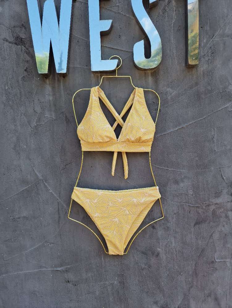 Yellow bikini set on a mannequin against a textured wall with 'WEST' sign.