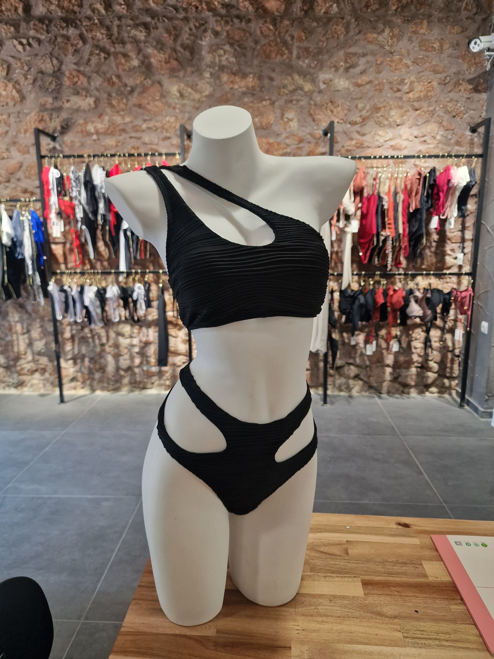 Mannequin wearing a black dress in a store setting with clothing racks in the background.

