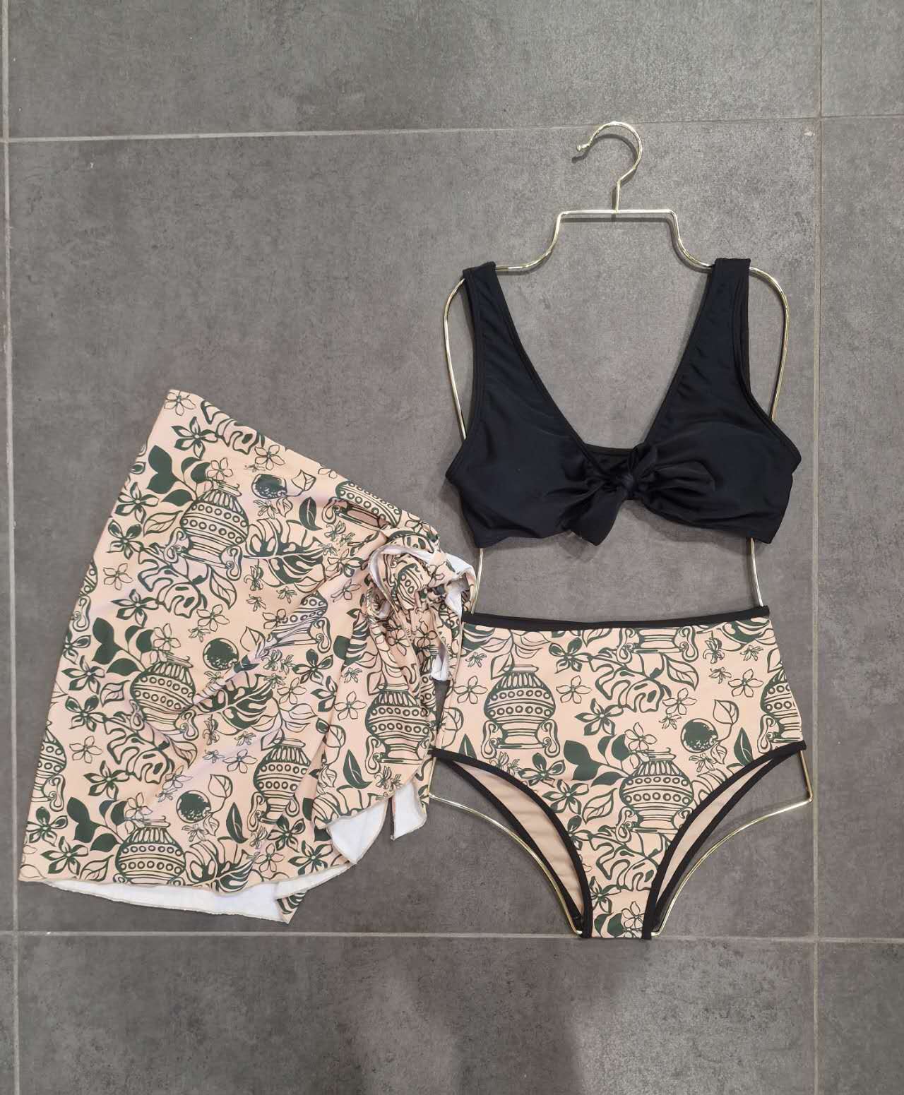 Black bikini top and patterned shorts on a hanger against a tiled wall.