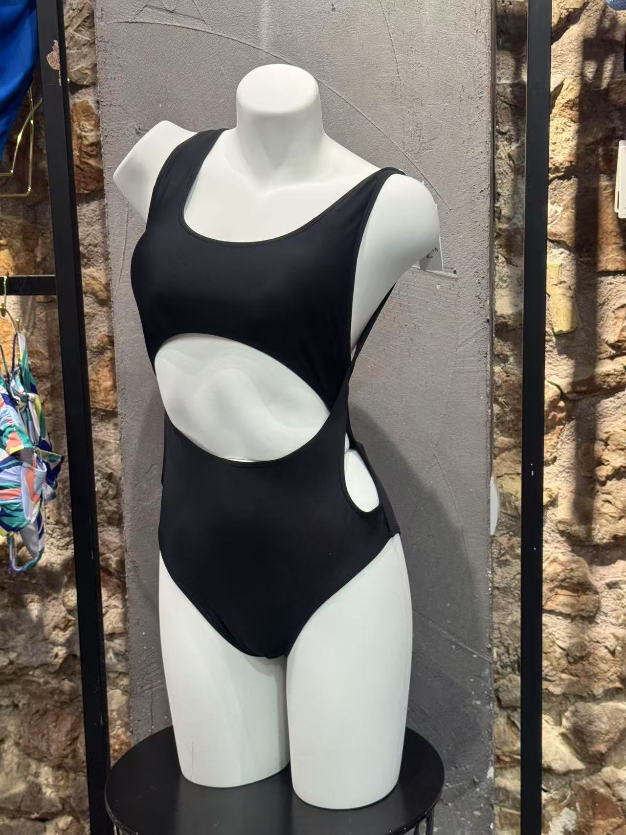 Black swimsuit on a mannequin against a stone wall.


