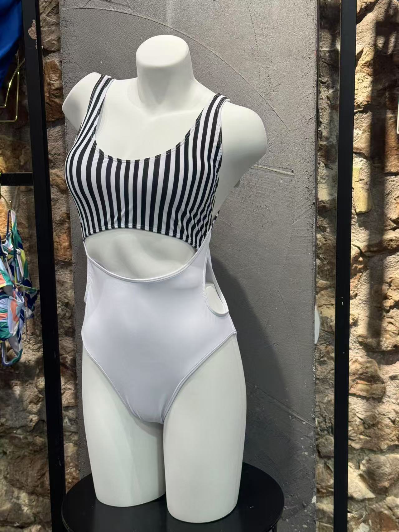 Mannequin wearing a black and white striped swimsuit against a stone wall.

