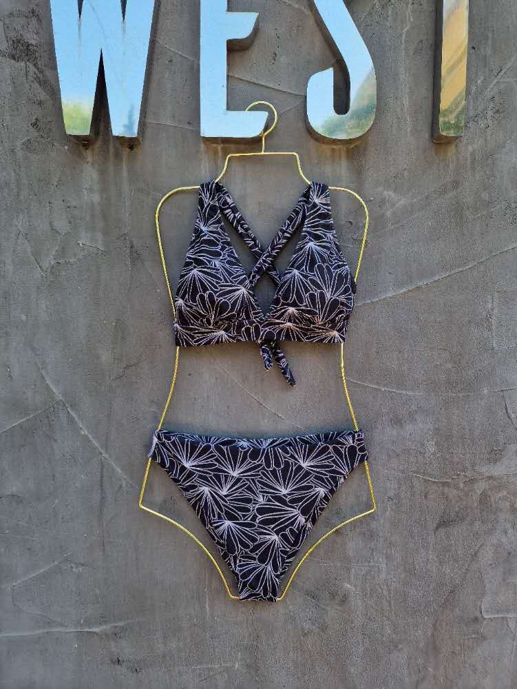 Bikini set on a hanger against a textured wall with 'WEST' letters.

