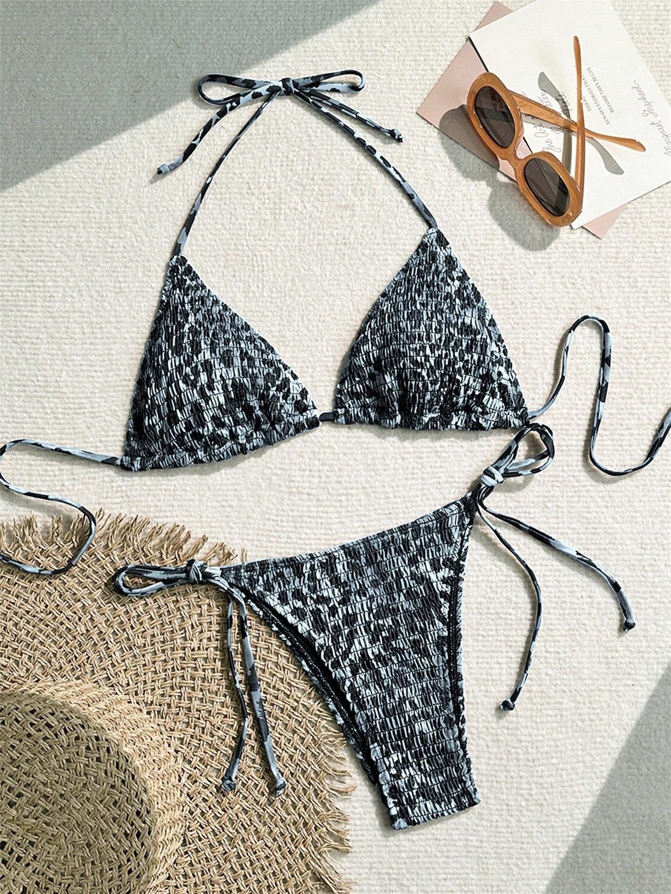 Black and white patterned bikini set with sunglasses and straw hat on a light surface

