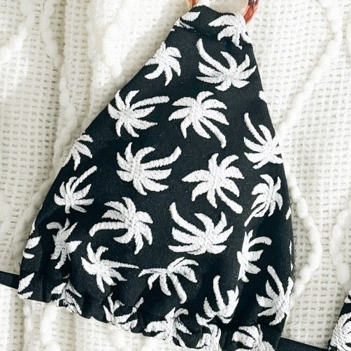 Black fabric with white palm tree pattern draped over a white textured surface

