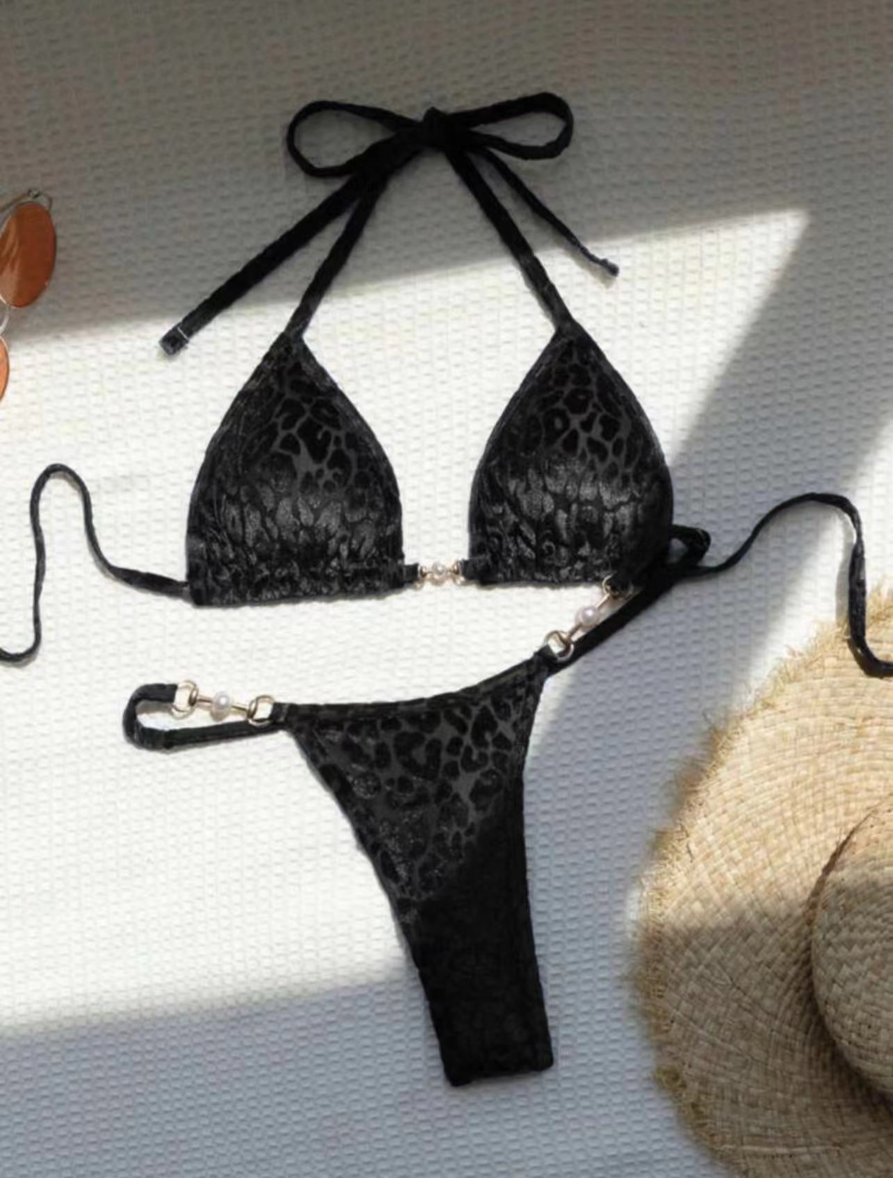 Black leopard print bikini set on a white surface with a straw hat and orange flower in the background.

