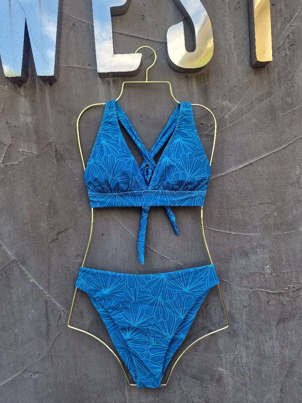 Blue bikini set on a mannequin against a textured wall.

