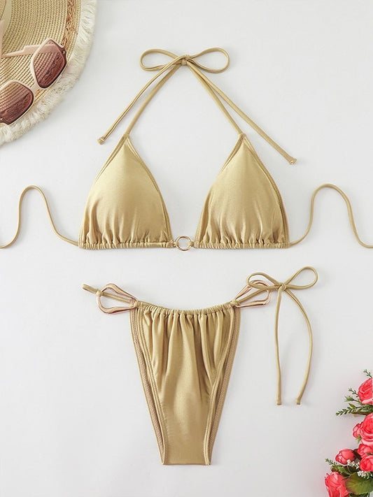 Gold bikini set on a white background with sunglasses and flowers.

