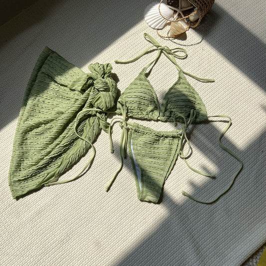 Green bikini set on a textured surface with sunlight casting shadows

