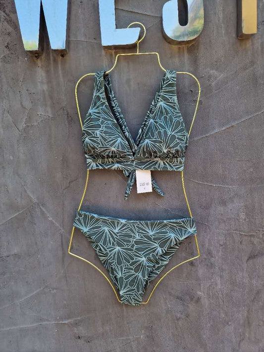 Green leaf-patterned bikini set on a hanger against a textured wall.


