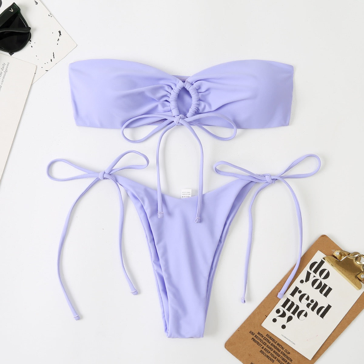 Lavender bikini set on a white background with a small brown box and black item.

