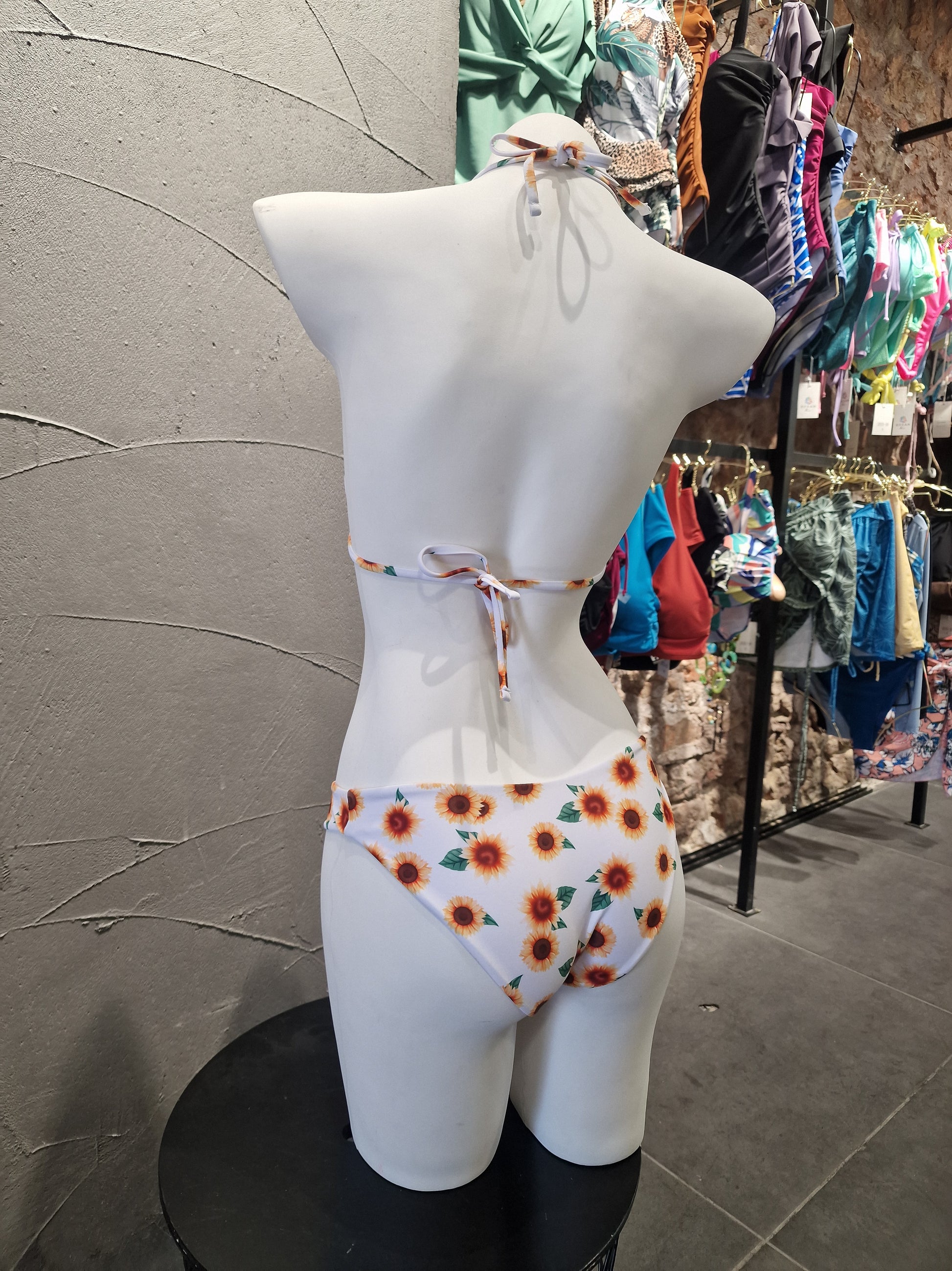 Mannequin wearing a floral-patterned dress with a blurred background of clothes on tables.

