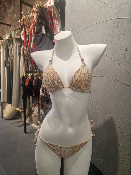 Mannequin wearing a white outfit with gold embellishments on a gray floor.

