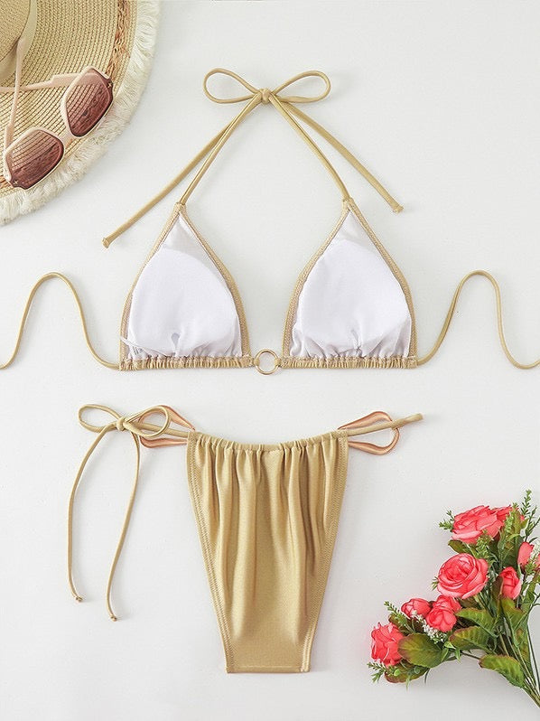 White bikini top with gold straps and matching bottom on a white background with flowers and a hat.

